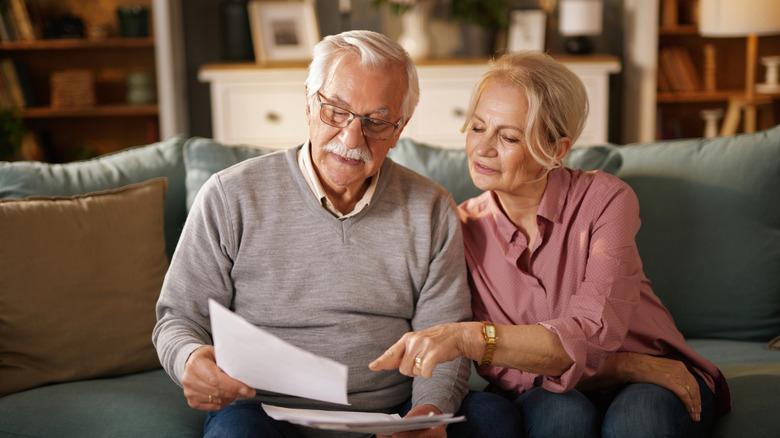 Senior aged couple sitting on couch in well-lit room reading a document