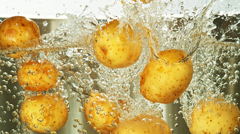 Whole potatoes falling into pot of boiling water