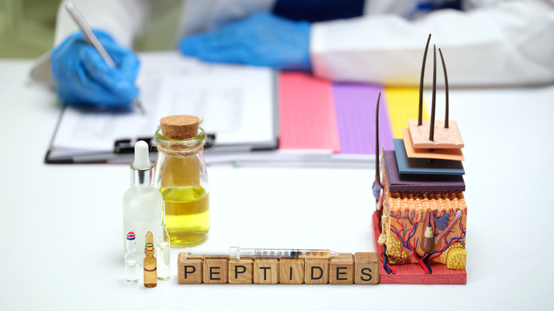 Block letters spelling out "peptides" propped up in front of a blurred researcher taking notes.