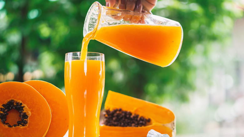 Hand pouring a glass of papaya juice next to sliced fruit