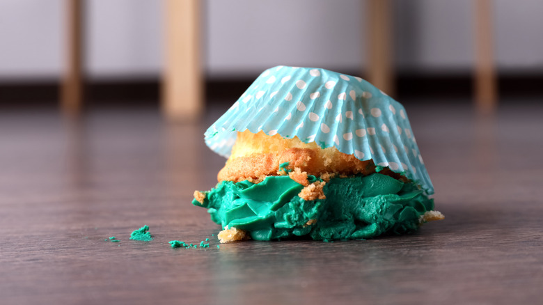 Cupcake with green frosting lying frosting side down on a wood floor