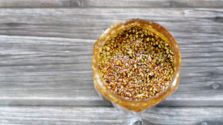 A glass of hundreds of small anise seeds floating in oil on wooden table