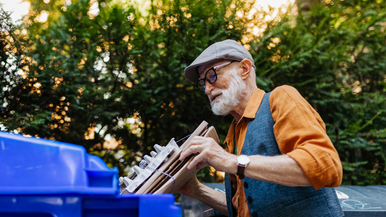Old bearded bespeckled man placing cardboard into recycling receptacle