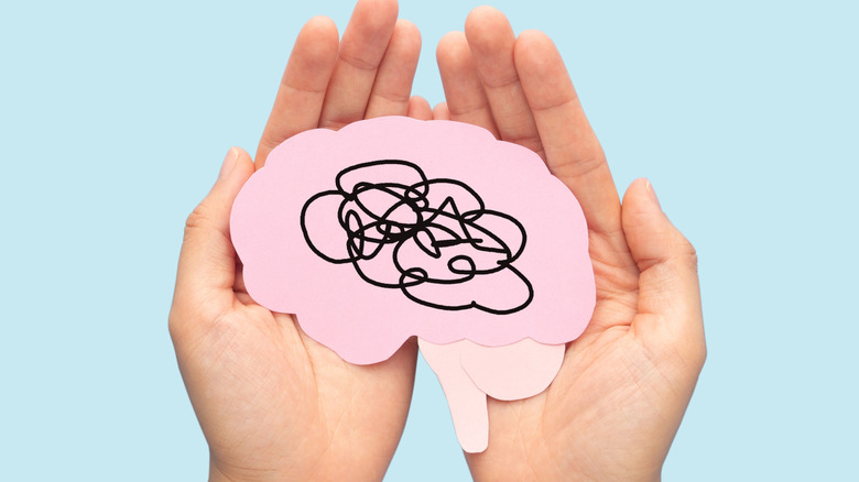 Pink cutout of a brain with scribbles on it in cupped hands on a blue background