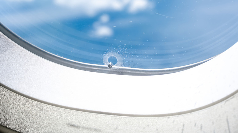 The bleed hole of a plane window is seen in closeup with a blue sky visible through the window pane