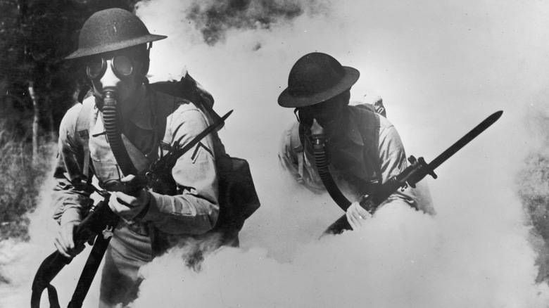 Two U.S. soldiers wearing gas masks while walking through plumes of smoke during World War I
