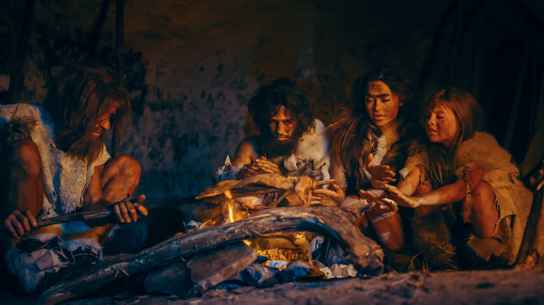 Four hunter gatherers cooking meat over a fire in a cave