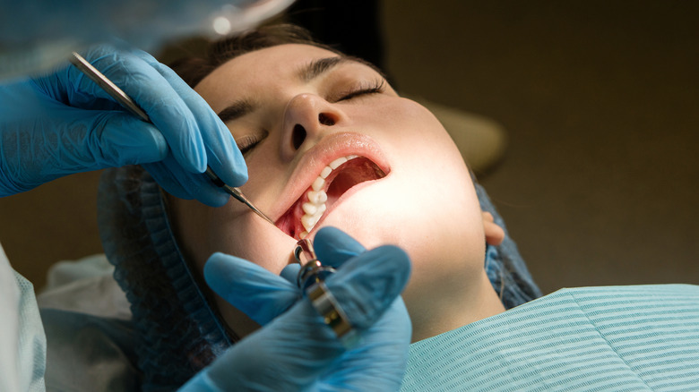 Dental surgeon operating on woman's mouth in a dentist chair
