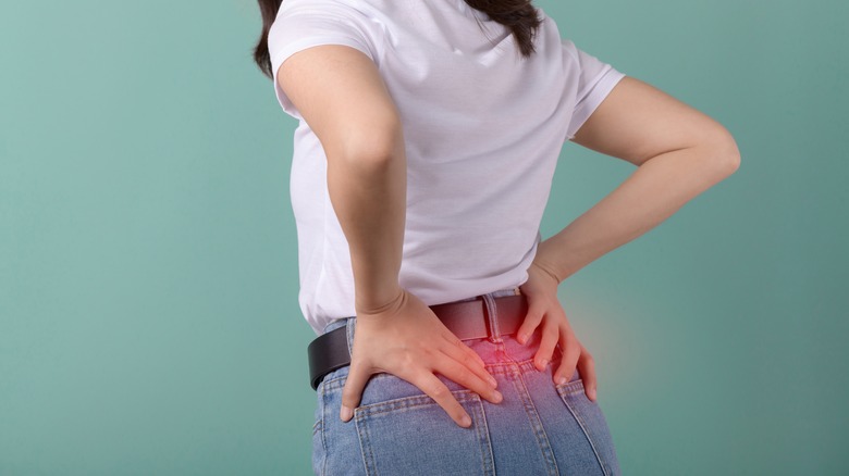 A woman hold her lower back in pain against a green background