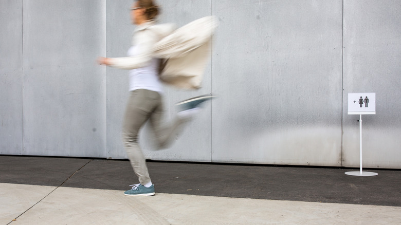 Woman running by with a sign pointing to a restroom in the background