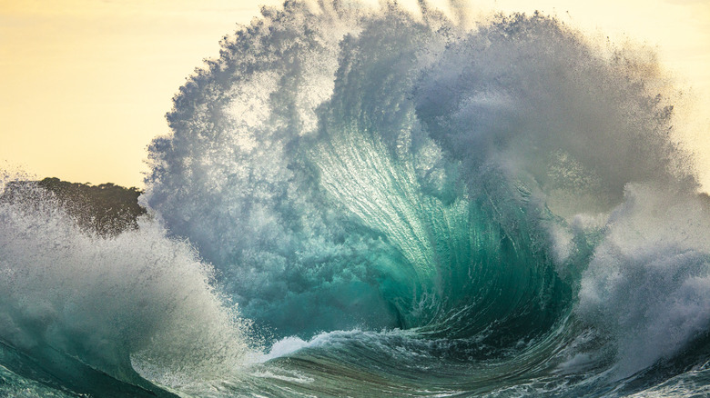 A very big wave beside a rocky shoreline.