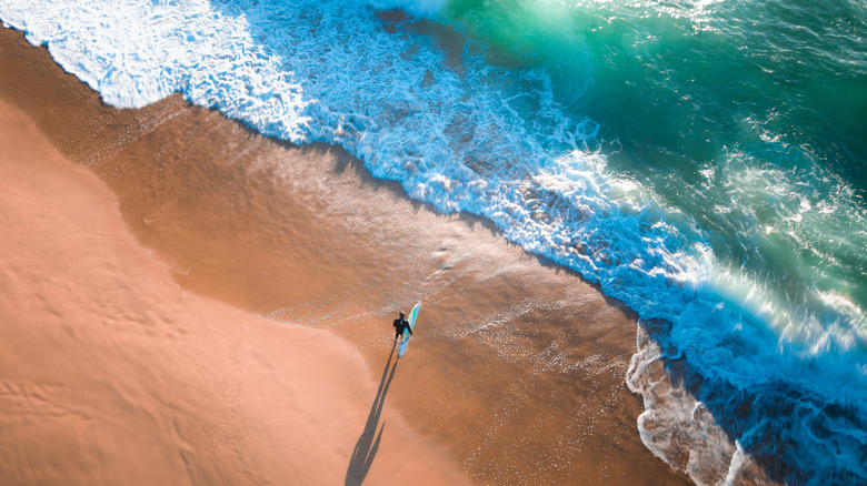 An aerial view of a surfer walking towards the ocean water.