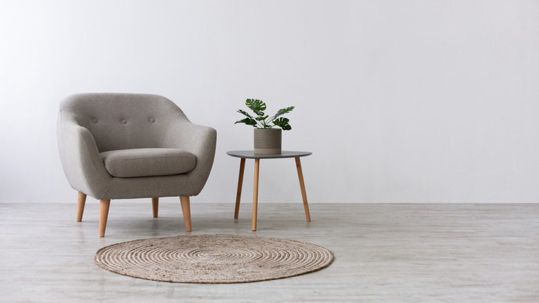 A chair, rug, and end table with a potted plant resting on top.