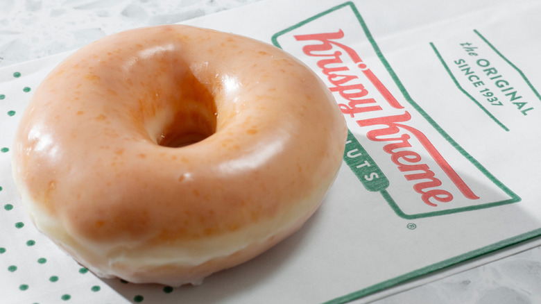 Close-up of a glazed Krispy Kreme donut sitting on the brand's paper bag