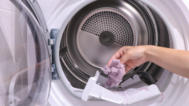 A woman's hand takes a lint trap out of a dryer