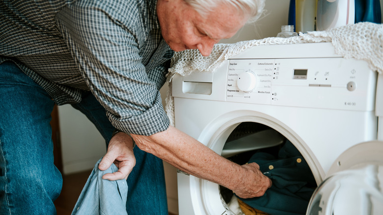 Elderly man loading clothes into a washing machine
