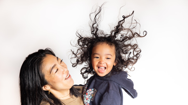 Mother holding toddler daughter, daughter's hair flung about