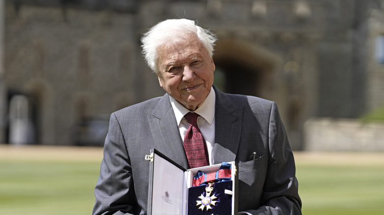 David Attenborough, old many smiling on castle lawn holding medal