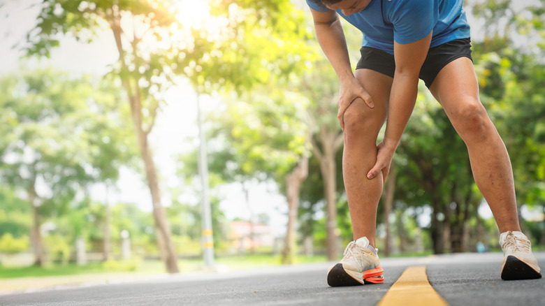 Athlete in shorts and running shoes outdoors leaning forward and grabbing leg