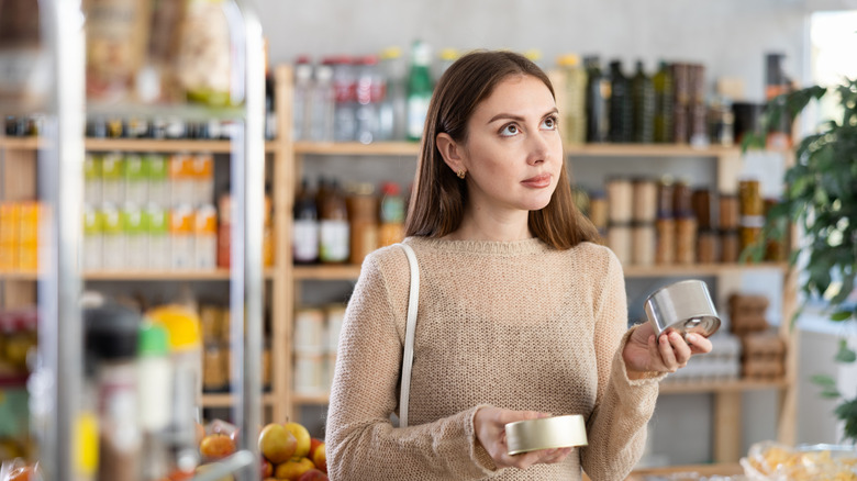 Woman holding two cans of food and contemplating the right choice