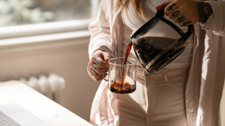 A woman with tattoos on her hands pouring herself a cup of coffee.