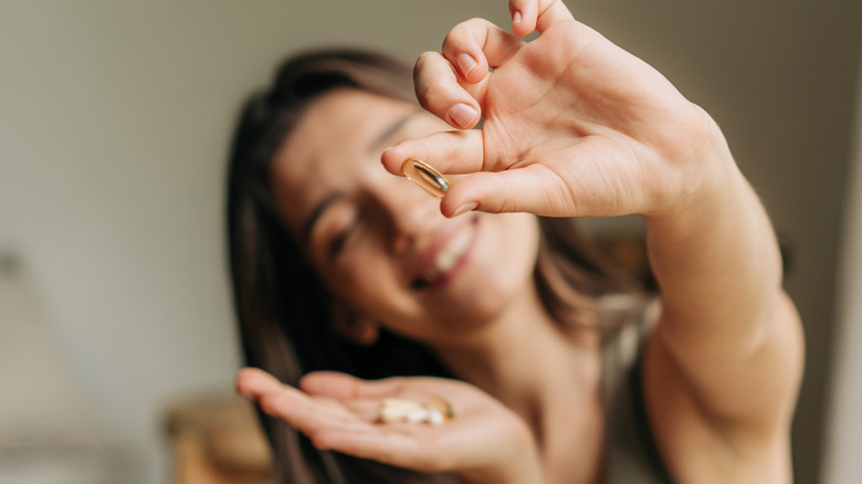smiling woman holds supplement capsule up, with several in other hand