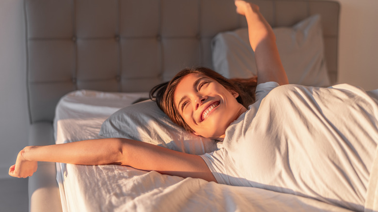 A woman waking up in the morning, stretching out her arms and smiling
