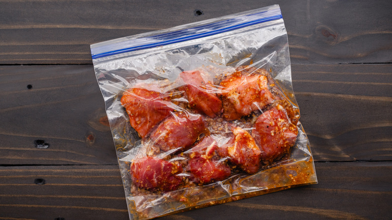Meat sits in a Ziploc bag on a wooden surface