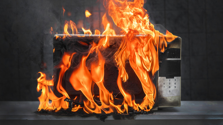 A microwave is shown on fire against a plain gray background