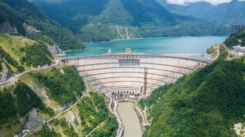 hydroelectric dam in valley, green wooded mountains, small river outlet below