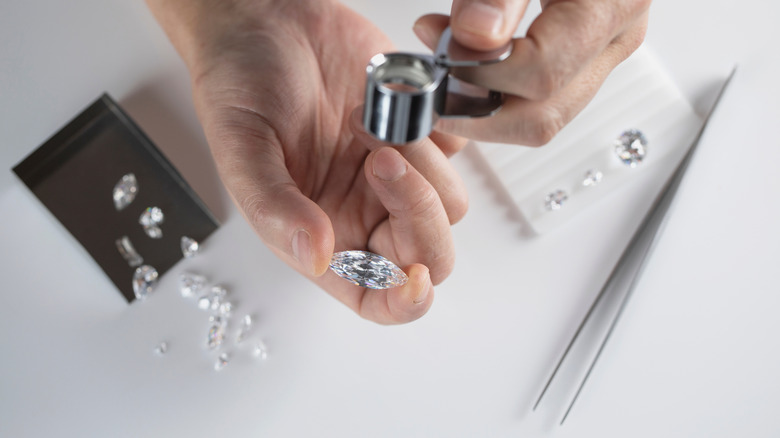 Clear gems held in hand with magnifying glass and tweezers