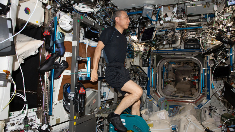 Japanese astronaut Furukawa pedals on a cycling machine while surrounded by equipment on the ISS