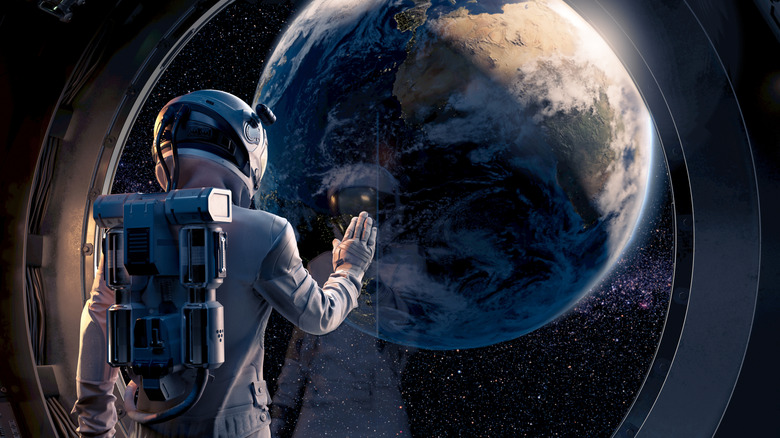 CGI of astronaut in space suit looking through circular window at Earth, hand on glass