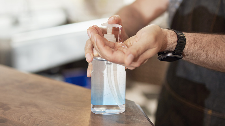 A man's hands are seen using a bottle of hand sanitizer resting on a countertop