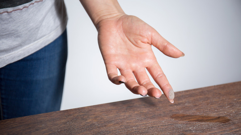 Woman running finger on dusty table in home