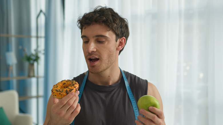 Man holding a donut and an apple