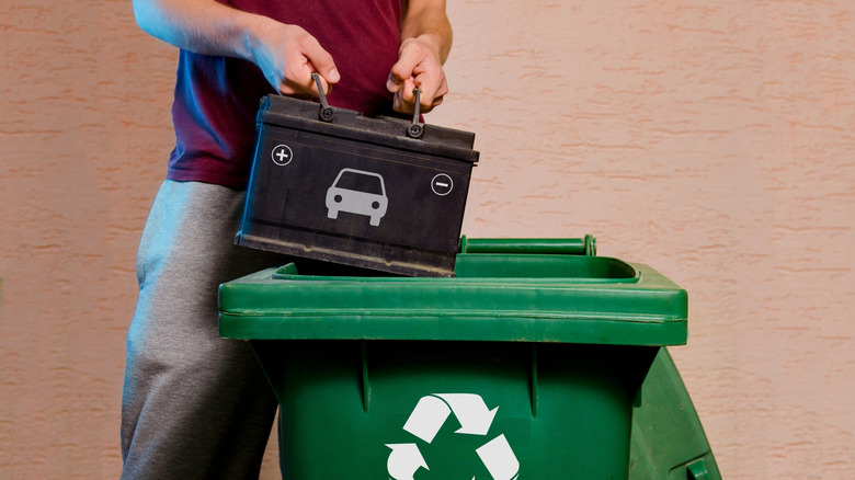 Man placing a traditional car battery into a green recycling bin