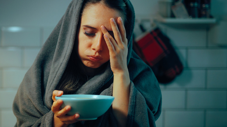 sick woman in kitchen with bowl of soup in hand