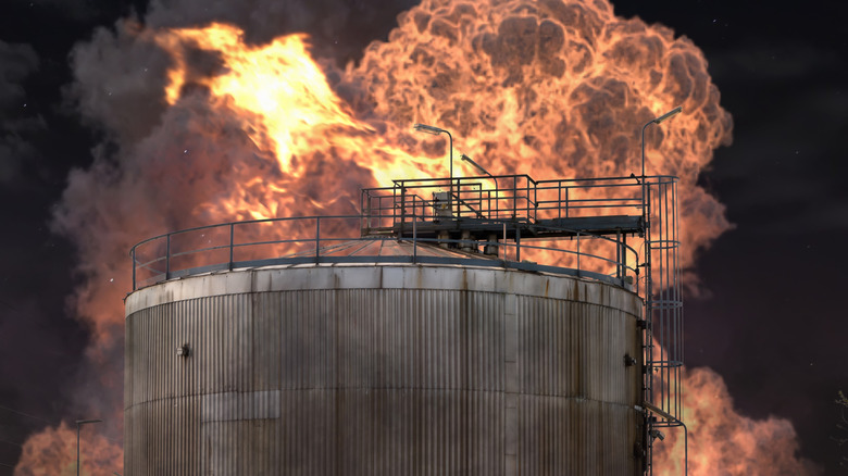 Oil refinery fire, large round oil depot in flames with black smoke