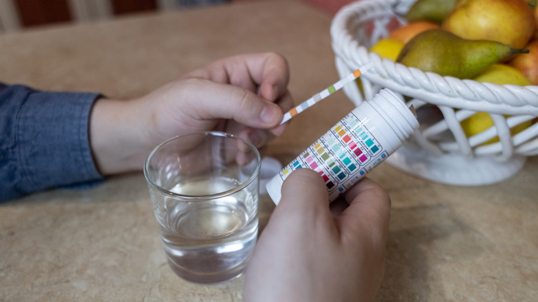 A man tests water quality in a kitchen using test strips