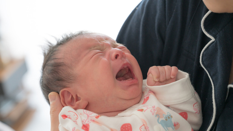 A newborn baby is crying while an adult holds him
