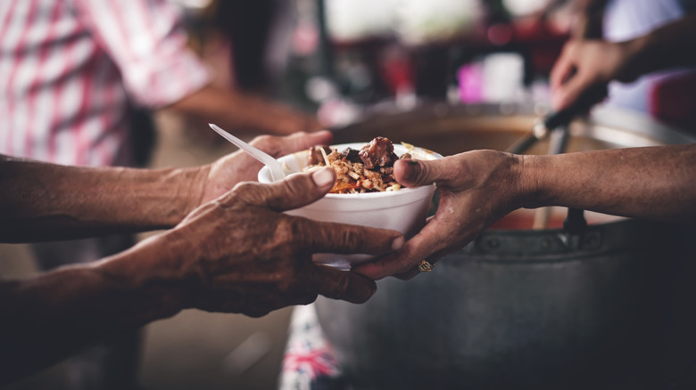 Hands are handing out a bowl of food