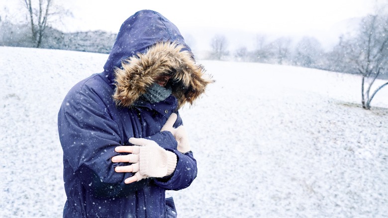 A person wearing winter clothing is shivering outdoors