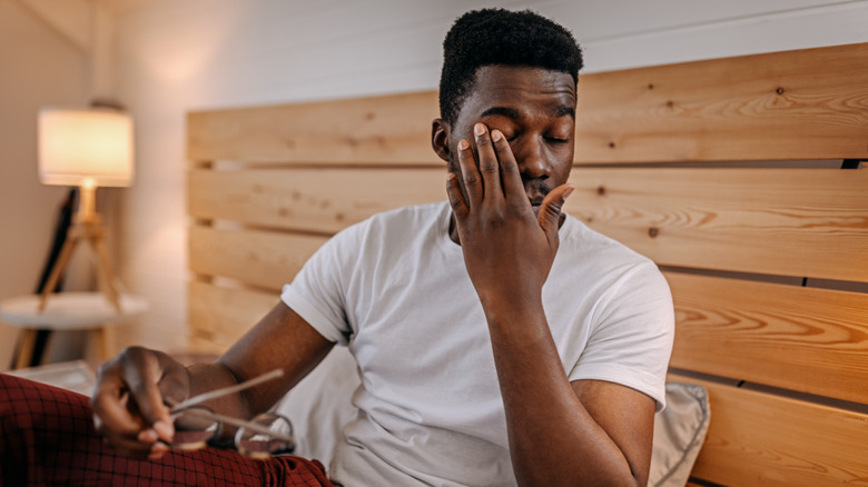 Man rubbing his eyes while sitting up in bed