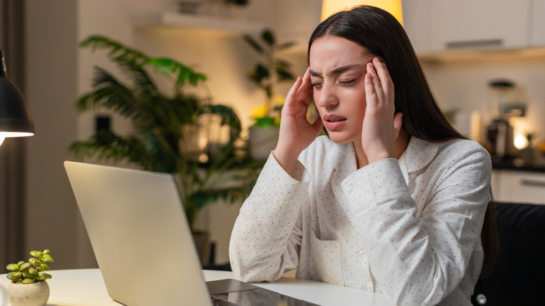 Woman sitting in front of computer screen and rubbing around eyes