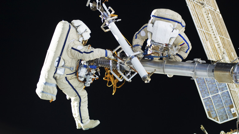 Two astronauts on the ISS during spacewalk, repairing arm