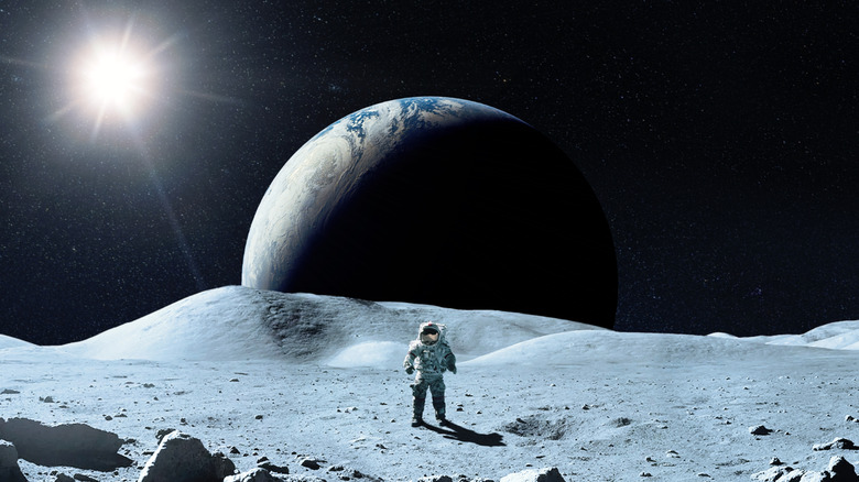 An astronaut stands on the Moon's surface with the Earth visible in the background