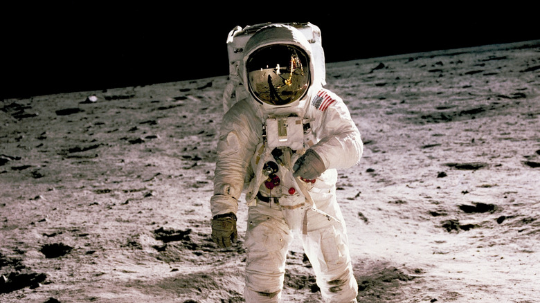 Edwin Aldrin is seen walking on the lunar surface with the reflection of Neil Armstrong, who took the photograph, visible in Aldrin's helmet visor