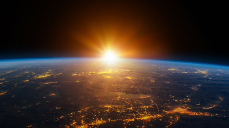 Sunrise over Earth, arching Earth with illuminated cities, sun casting orange beams