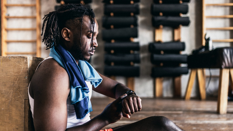 Man sitting in a gym while checking smartwatch